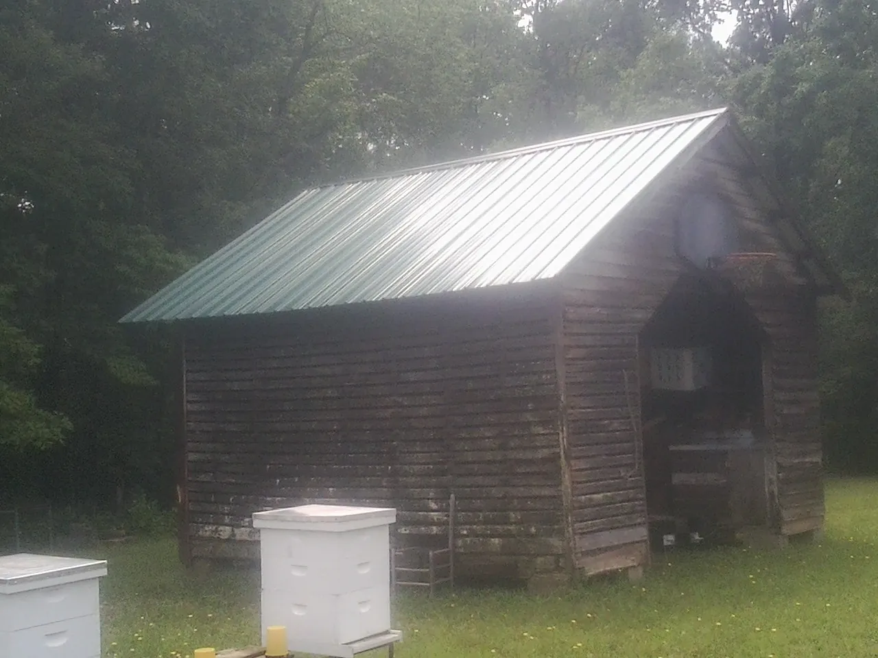 Green metal roof on a weathered barn beside stacked beehives in Winchester